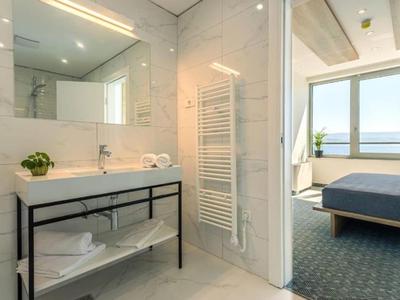 Helles Bad mit Waschbecken, Handtüchern und Blick auf ein Zimmer mit Meerblick.