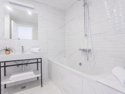 Modernes, helles Badezimmer mit weißen Fliesen, Badewanne und Waschbecken.