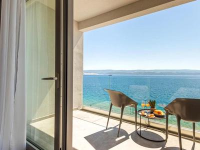 Balkon mit zwei Stühlen und Tisch mit Getränken, Blick auf das blaue Meer und den klaren Himmel.