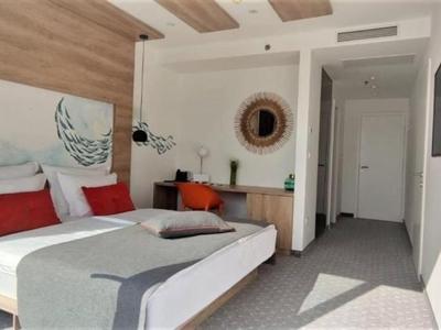 Helles Hotelzimmer mit Doppelbett, roten Kissen, Flachbildschirm und modernem Dekor.