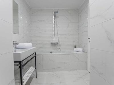 Modernes Badezimmer mit weißem Marmor, Badewanne, Duschkopf und Handtüchern.