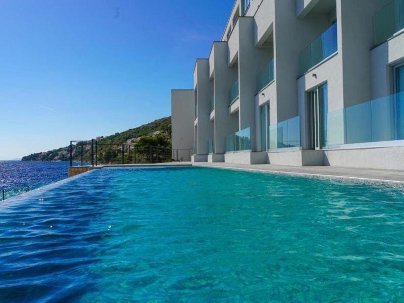 Infinity-Pool neben modernem Hotelgebäude mit Meerblick und blauem Himmel.