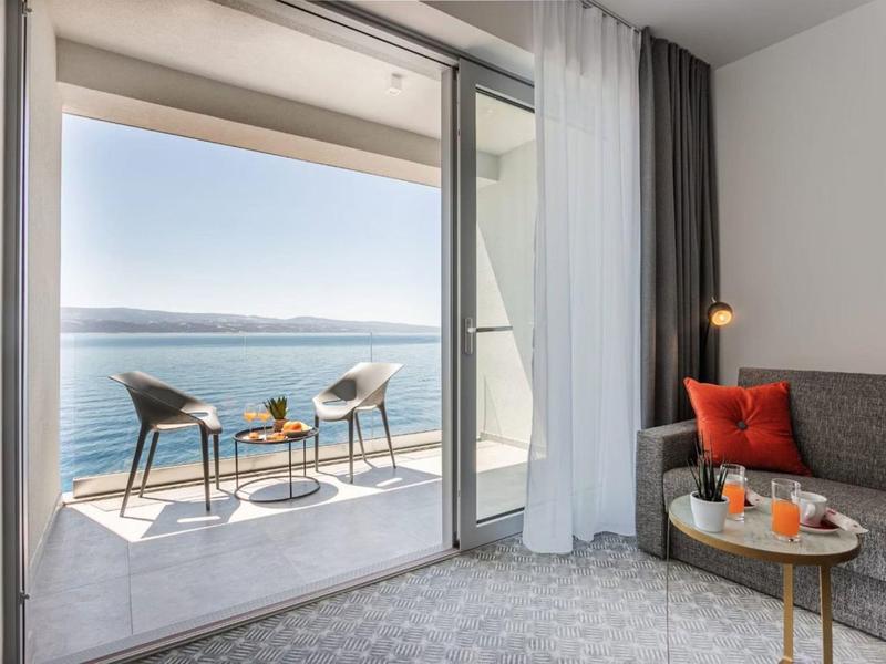 Moderner Hotelzimmer mit Balkon und Blick auf das Meer mit Stühlen und Tisch.