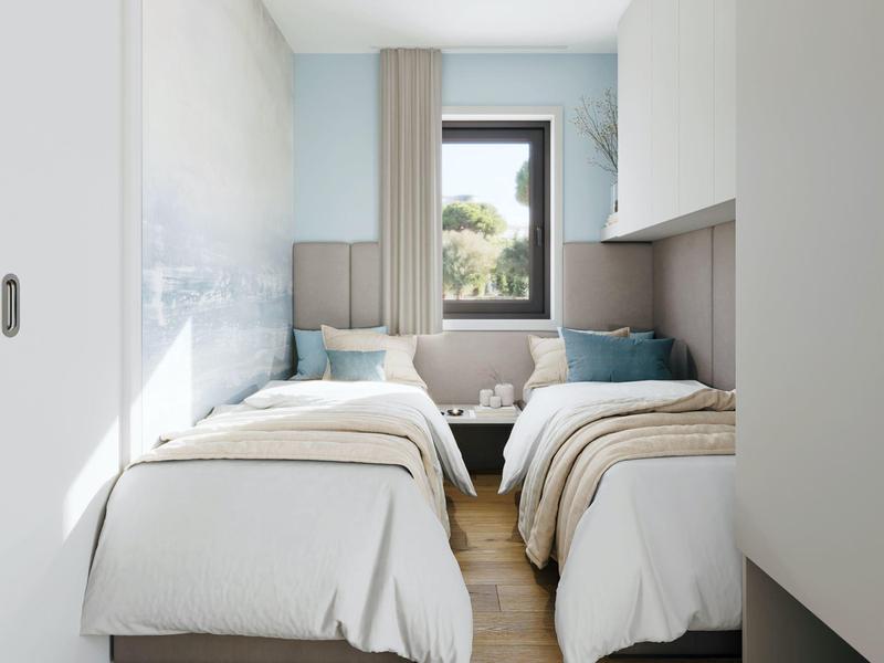 Světý pokoj s dvěma jednolůžky, šedými čely postelí a oknem s výhledem na zeleň.