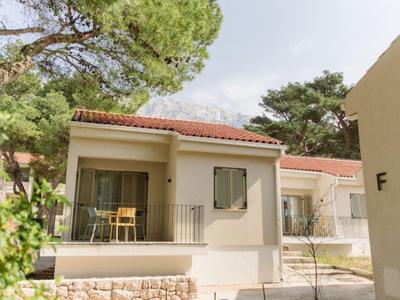 Modern holiday home with terrace, chairs and table, surrounded by trees and clear sky.