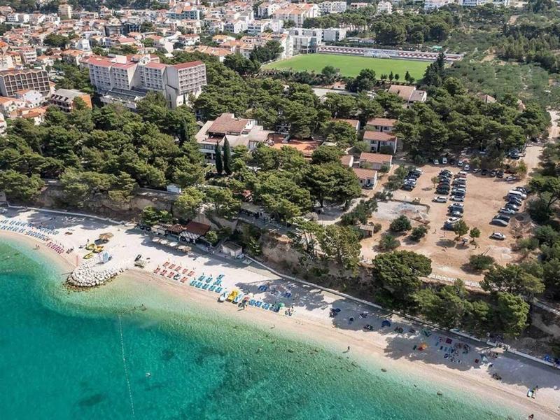 Vue aérienne d'une ville côtière avec plage de sable, eau turquoise et arbres.
