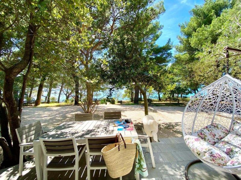 Espace de détente extérieur avec table, chaises et fauteuil suspendu dans un jardin ombragé près de l'eau.