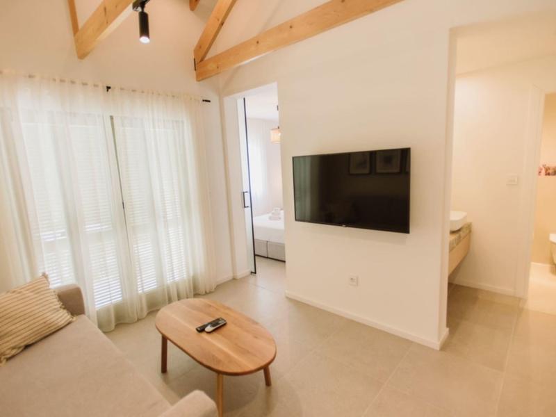 Salon lumineux avec canapé, table en bois, télévision murale et poutres apparentes au plafond.