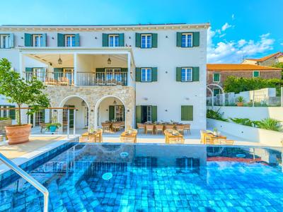 Mehrstöckiges weißes Ferienhaus mit Terrasse und blauem Swimmingpool im Vordergrund.