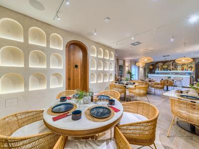 Modernes Restaurant mit runden Tischen, geflochtenen Stühlen und dekorativer Wandbeleuchtung.