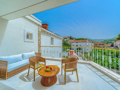 Balkon mit Sitzgruppe aus Korbmöbeln und Blick auf andere Häuser und Hügel.