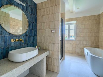 Modernes Badezimmer mit ovalem Spiegel, Waschbecken auf Steinplatte und freistehender Badewanne.