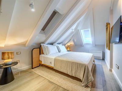 Schlafzimmer mit Dachschräge, weißem Bett und modernem Dekor in warmen Tönen.
