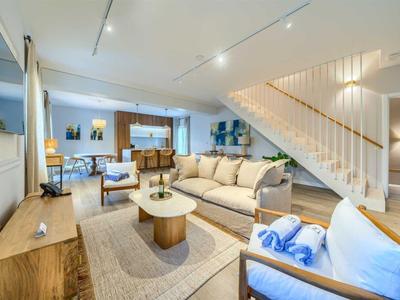 Hell eingerichtetes Wohnzimmer mit Sofa, Sesseln und moderner Treppe im Hintergrund.
