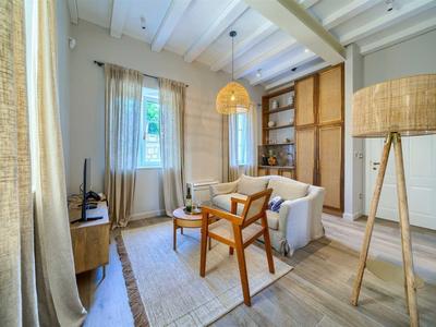 Helles Wohnzimmer mit Holzstuhl, Sofa und Stehlampe neben Fenster und Vorhängen.