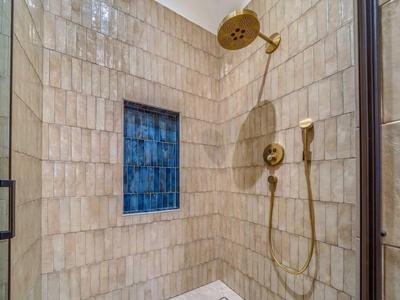 Moderne Dusche mit goldfarbenem Duschkopf und handlicher Brause in cremefarben gefliestem Bad.
