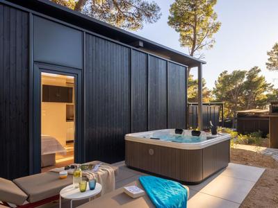 Moderner Außenbereich mit Whirlpool auf Terrasse neben Holzhütte in sonniger Umgebung.