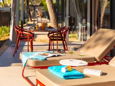 Zwei Liegestühle mit blauen Handtüchern und Gläsern auf einem sonnigen Hotelbalkon mit Tisch und Stühlen.