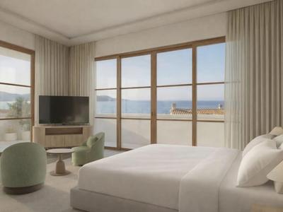 Helles Hotelzimmer mit großem Bett, Sitzbereich und Panoramafenstern zum Meer.