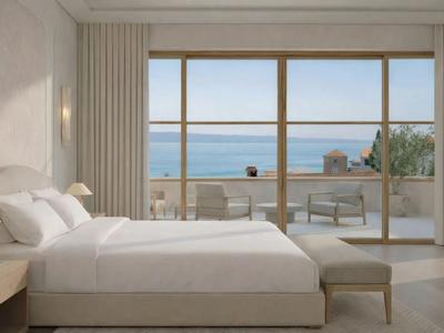 Helles Hotelzimmer mit großem Bett und Meerblick durch bodentiefe Fenster.