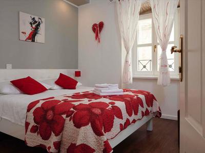 Gemütliches Hotelzimmer mit Doppelbett, roten Akzenten und hellem Fenster mit weißen Vorhängen.