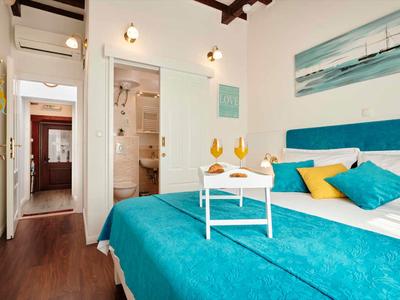 Modernes Hotelzimmer mit Doppelbett, blauem Bettüberwurf, Holzfußboden und Bad mit Dusche.
