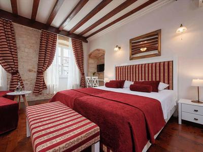 Gemütliches Hotelzimmer mit Doppelbett, roten Vorhängen und Holzbalkendecke.