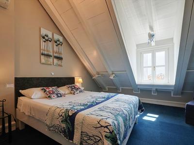 Hell eingerichtetes Hotelzimmer mit Doppellbett, Dachschräge und Fenster mit Blick nach außen.