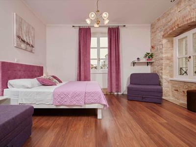Gemütliches Hotelzimmer mit Holzboden, violetten Vorhängen und Sitzgelegenheiten neben Fenstern.