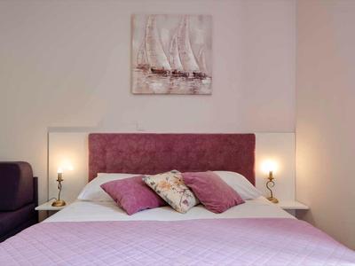 Modern eingerichtetes Schlafzimmer mit lilafarbenem Bett, Kissen und indirekter Beleuchtung.