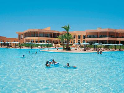 Hotel mit großem Außenpool, klar blauem Wasser und Menschen beim Schwimmen unter klarem Himmel.