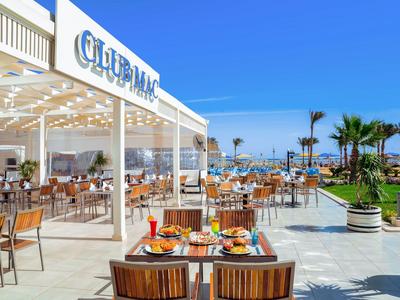 Außenrestaurant mit Holztischen und Blick auf den Pool in einem Hotel bei klarem Himmel.