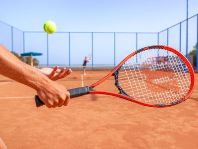 Ein Tennisspieler trifft einen gelben Ball auf einem roten Sandplatz bei klarem Himmel.