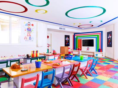Bunter, heller Kinderspielraum mit kleinen Stühlen, Tischen und buntem Teppich.