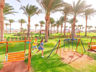 Kind spielt auf einem sonnigen, gepflegten Spielplatz mit Palmen in einem Hotelresort.