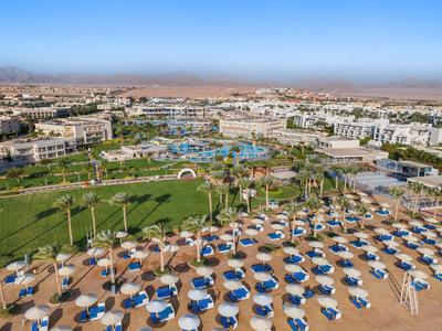 Großer Hotelkomplex mit mehreren Pools, Sonnenschirmen und Liegestühlen in einer sonnigen Landschaft.