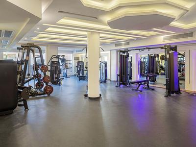 Großer, moderner Fitnessraum mit Trainingsgeräten und heller, indirekter Beleuchtung.
