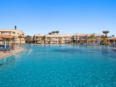 Großer Hotelpool mit klarem Wasser, Sonnenliegen und zweistöckigen Hotelgebäuden im Hintergrund.