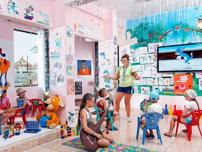 Hell gestalteter Spielraum mit Kindern, Betreuerin und bunten Möbeln in einem Hotel.