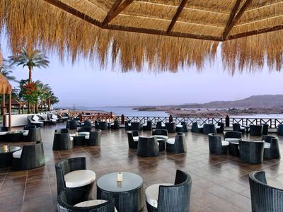 Offene Terrasse mit Strohschirm, dunklen Sitzmöbeln und Blick aufs Meer und die Berge.