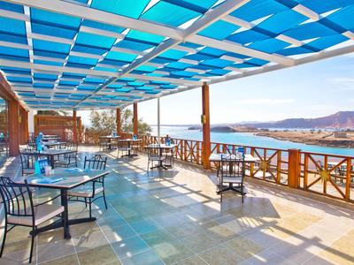 Große Terrasse mit Sitzgelegenheiten und Panoramablick auf das Meer und die Berge bei Sonnenschein.
