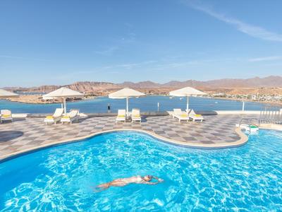 Ein Outdoor-Pool mit klarem blauem Wasser, Liegestühlen und Sonnenschirmen am Ufer unter blauem Himmel.