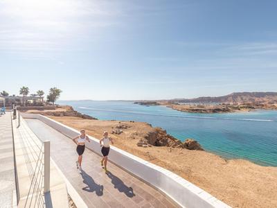 Zwei Frauen joggen auf einem Weg entlang der Küste mit Blick aufs Meer und goldene Hügel.