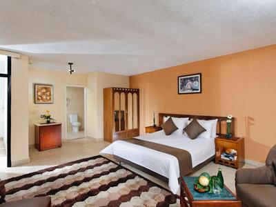 Modern eingerichtetes Hotelzimmer mit großem Bett, Teppich und Balkon mit Sitzbereich.