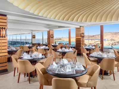Elegantní restaurace s moderním nábytkem a panoramatickými okny s výhledem na pouštní krajinu.