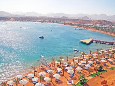 Küstenhotel mit blauen Sonnenschirmen, Liegestühlen und Booten im klaren Meer am Strand.