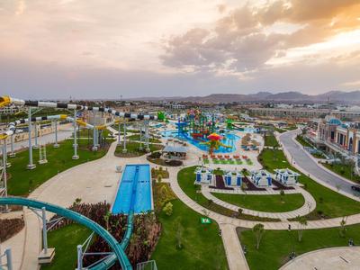 Großer Wasserpark mit Rutschen, Pools, Wegen und Grünflächen unter bewölktem Himmel.