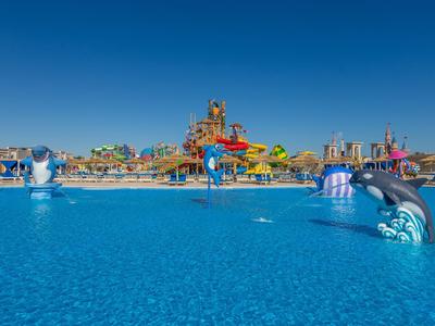Großes Schwimmbecken mit Wasserspielen und farbenfrohen Rutschen unter klarem blauen Himmel.