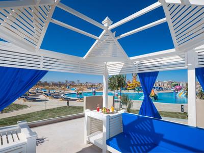 Offener Pavillon mit blauem Himmel, blauem Vorhang und Blick auf Pool und Hotelbereich.