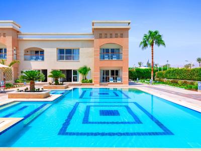 Moderner Hotelpool mit klarem Wasser, Sitzbereichen und Palmen unter blaugem Himmel.